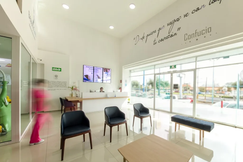 Sala de espera de la clínica: sillones oscuros y mesa baja, mostrador de recepción al fondo y ventanal a la calle.